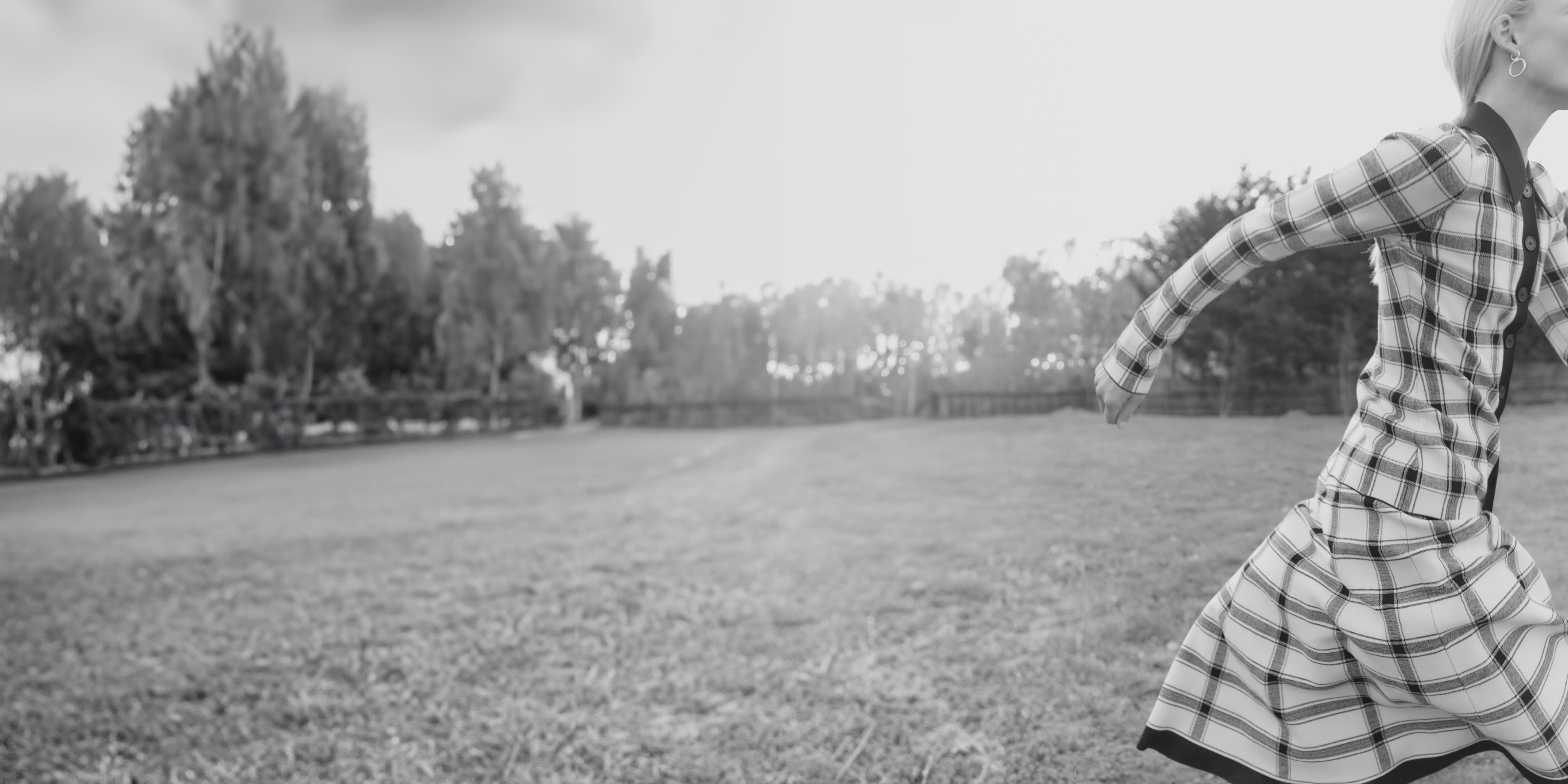 black and white image of woman wearing plaid knit top + skirt set, running off the side of the image