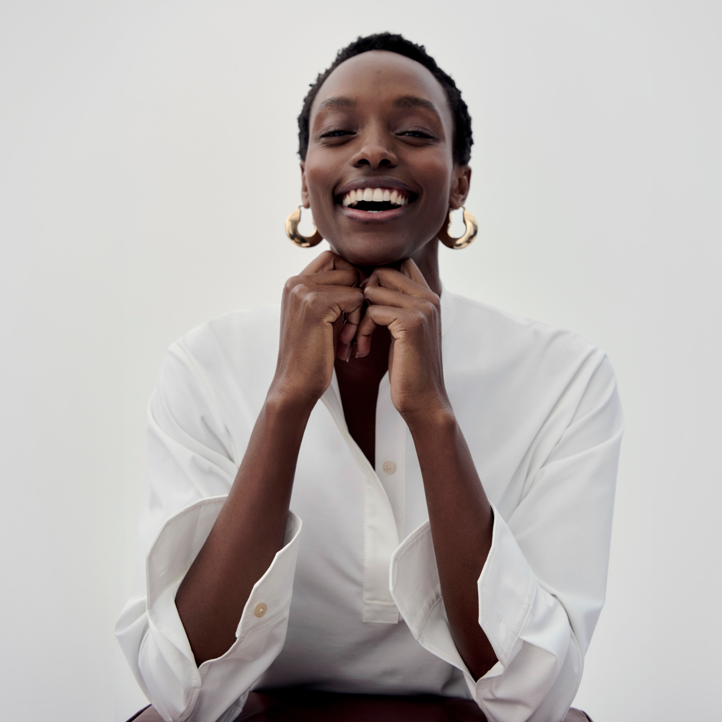 woman resting her chin on her hands and smiling, wearing white top