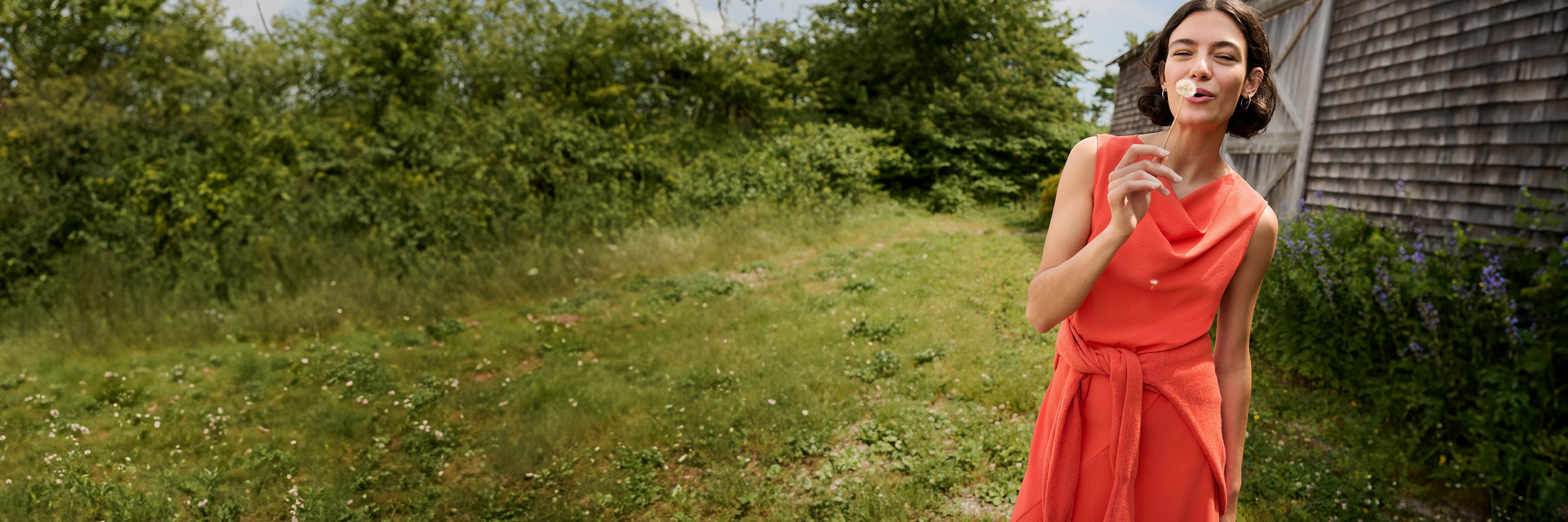 image of a woman wearing the priya dress in bright coral