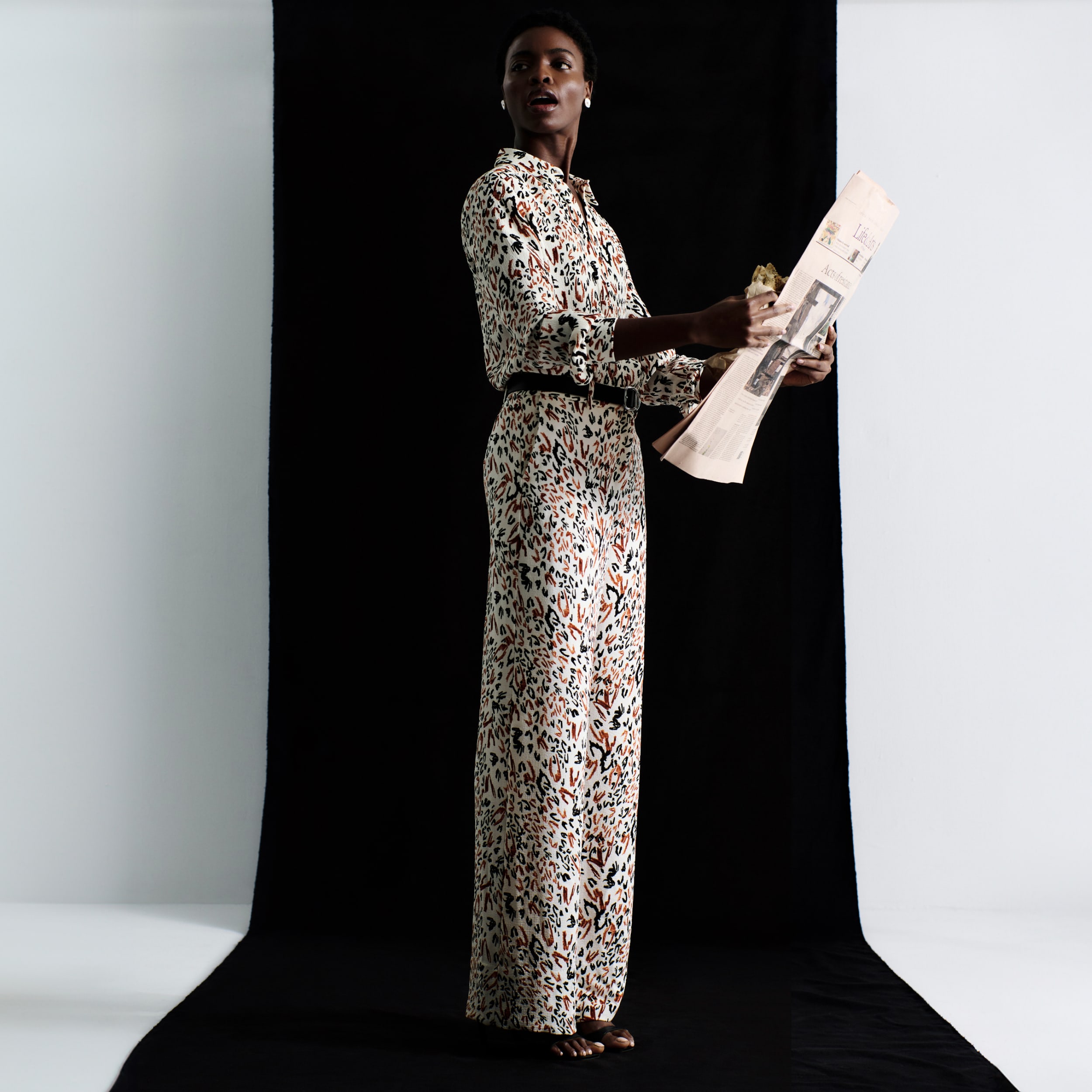 woman wearing Lagarde button-up shirt and wide-leg Tinsley trouser in matching leopard sketch print, holding a newspaper and looking over her shoulder