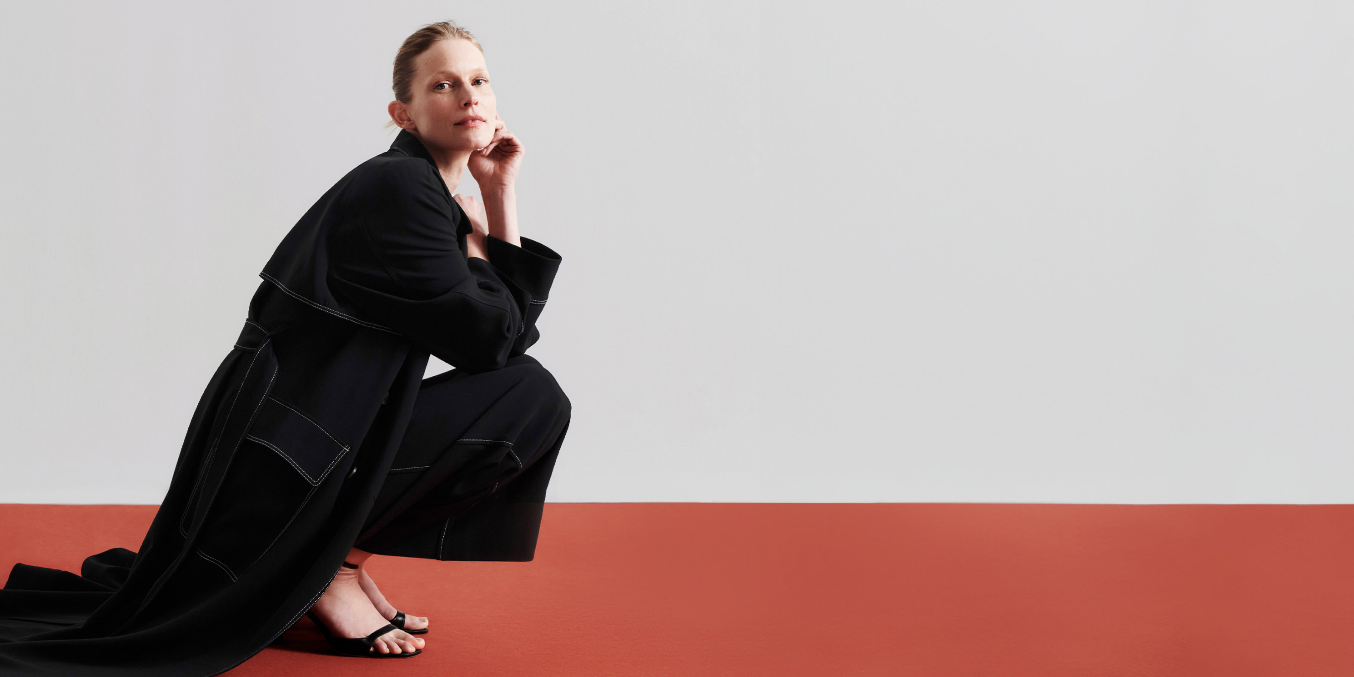 woman wearing black Trench coat crouching down on red floor