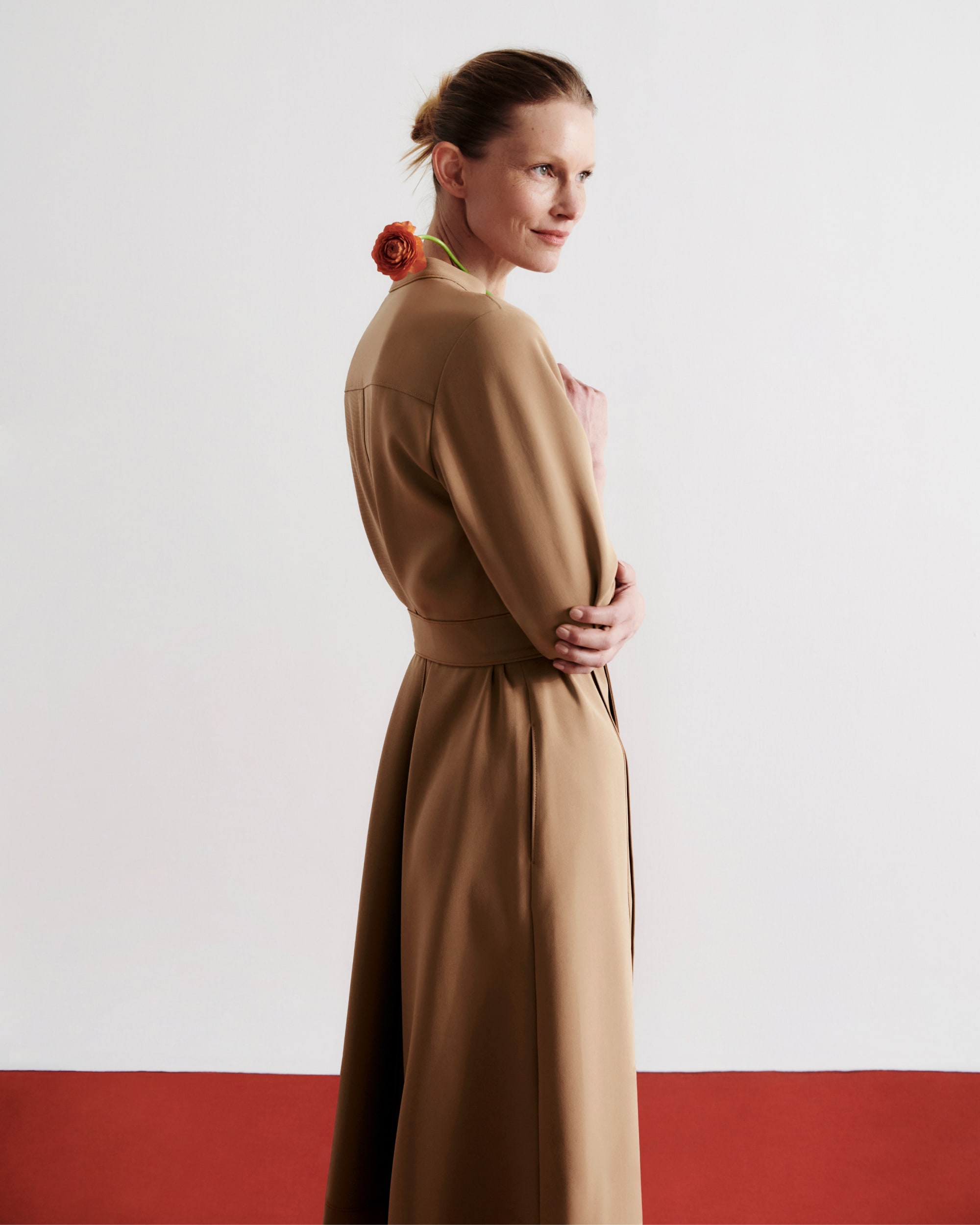 image of a woman holding a flower over her shoulder wearing the lauleh dress in light saddle