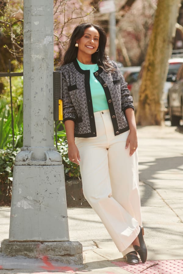 woman standing outside leaning against a streetpole, wearing M.M.LaFleur knit Evangeline jardigan, seafoam Leslie T-shirt, and white wide-leg Milo jeans