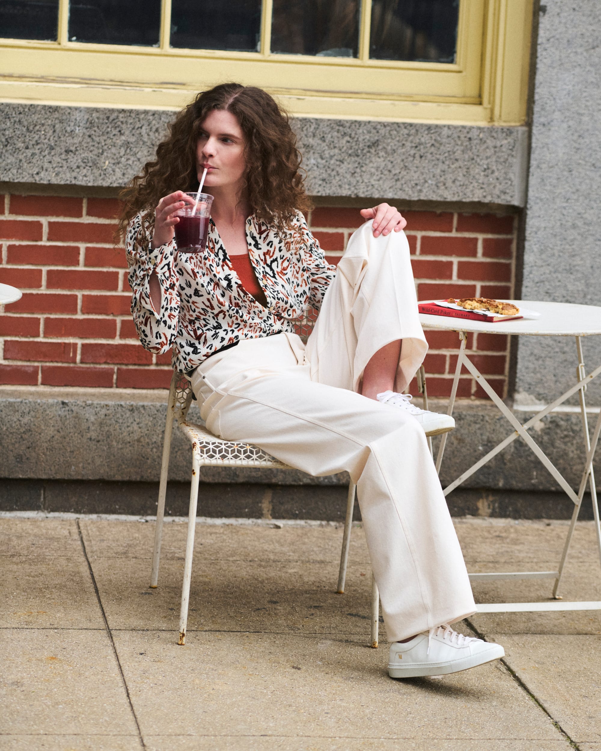 image of a woman sitting wearing a patterned top and ivory jeans