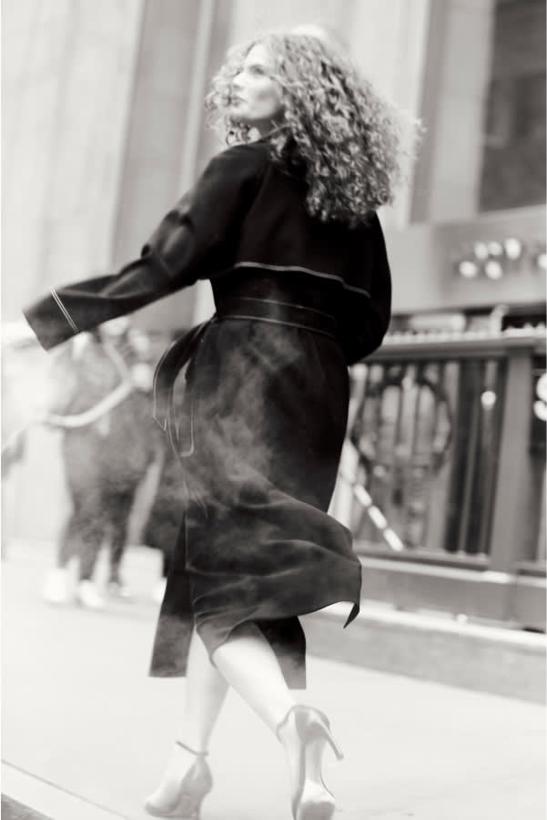 black and white image of back of woman wearing black Frankie trench coat walking down street