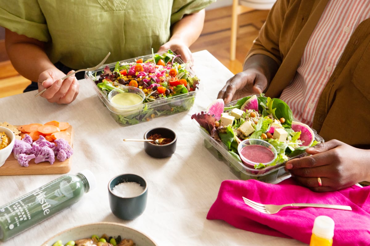 table shot of two people about to eat a salad with dressings and green juices on the table
