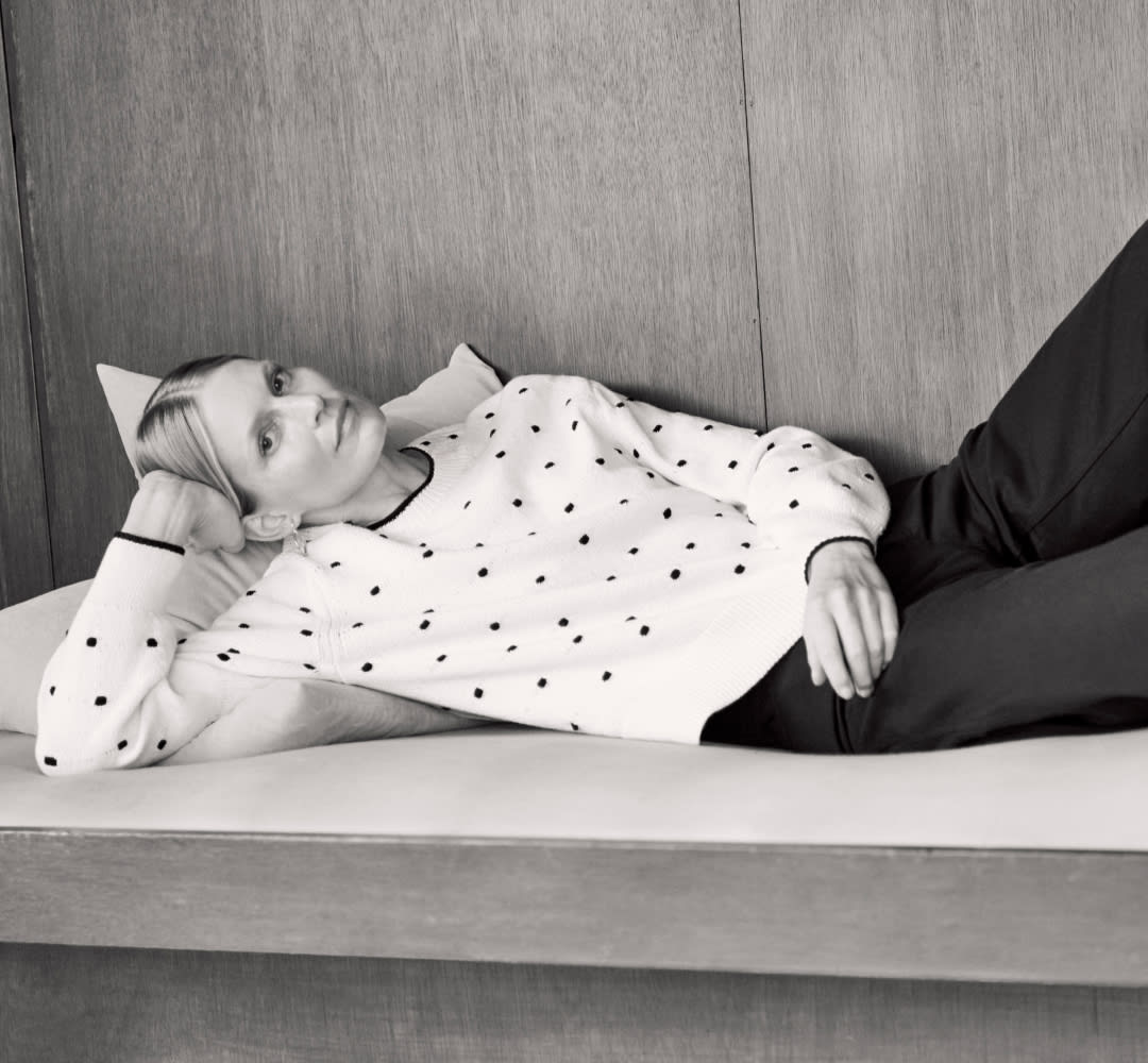 black and white image of woman laying down resting her head in one hand, wearing white sweater with black knitted dot pattern