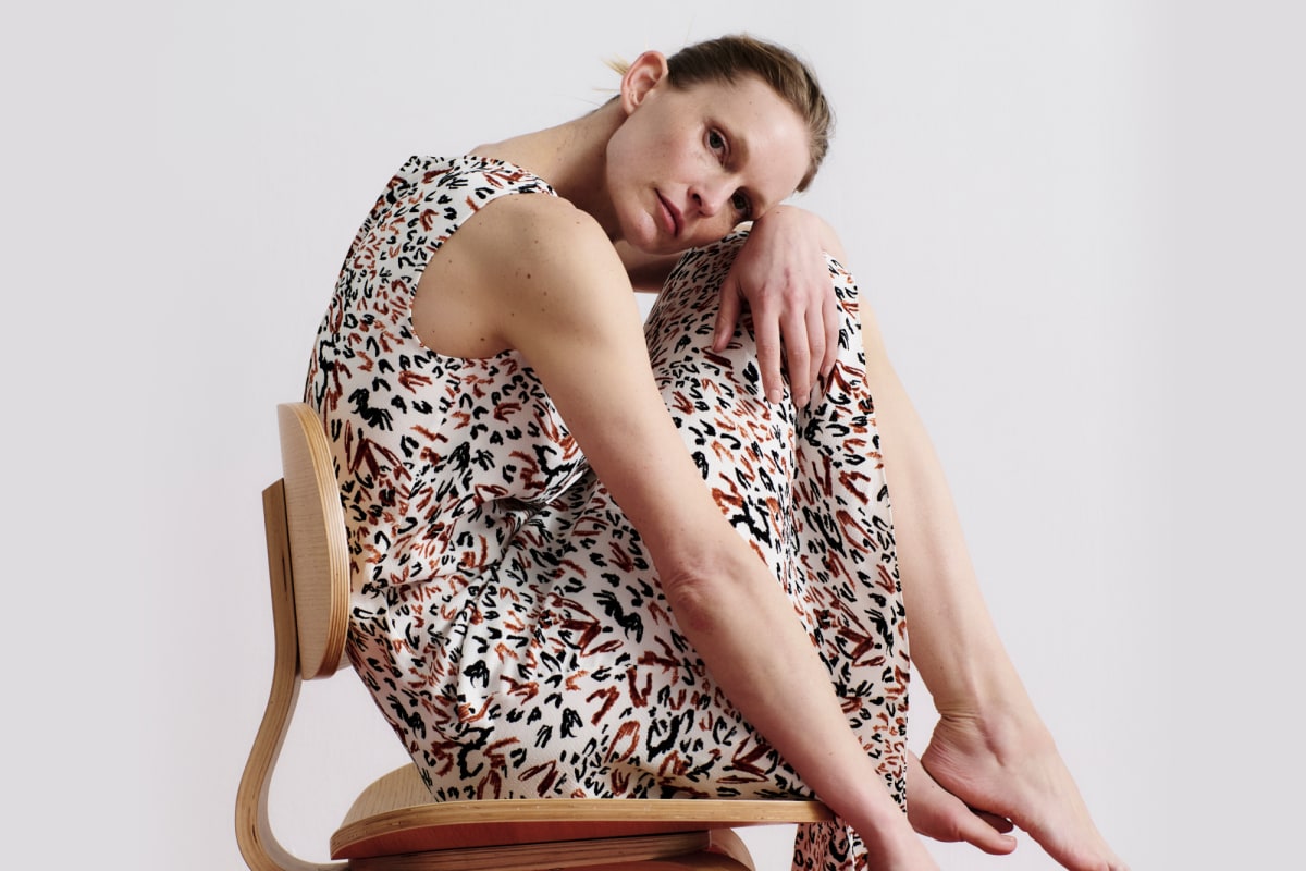 woman wearing sleeveless dress sitting in chair in front of light grey background