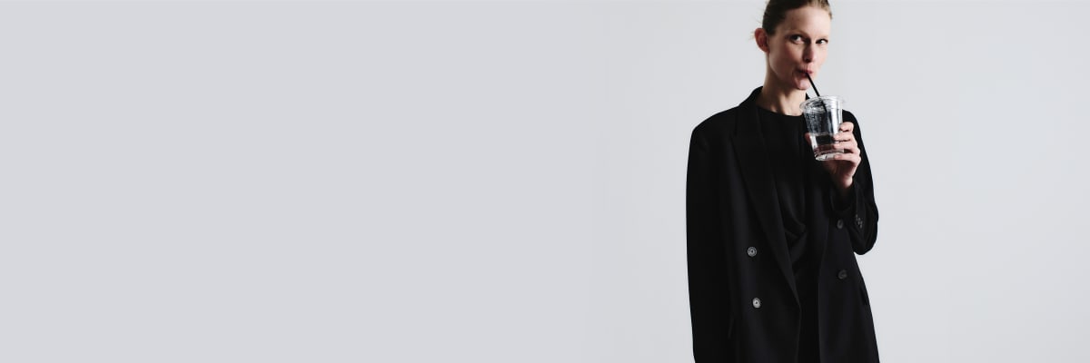 woman wearing black blazer and sipping water from clear cup