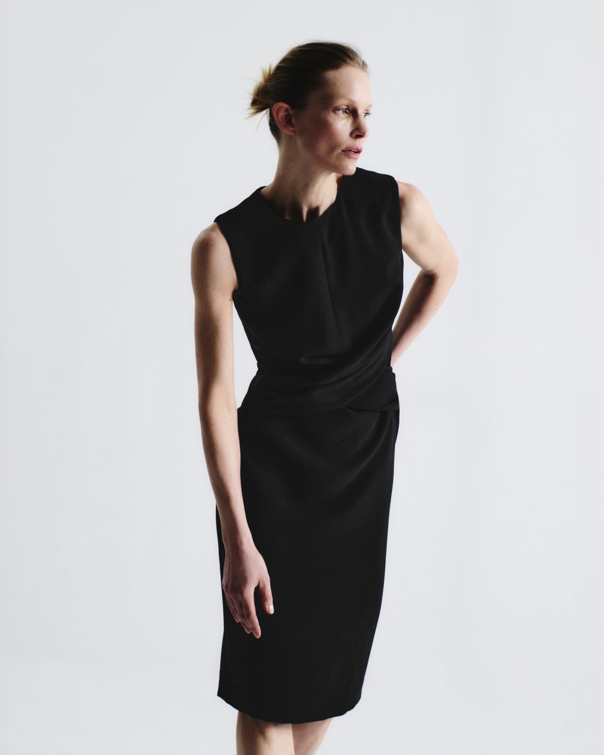 woman wearing sleeveless black Luz dress with one hand on her hip and leaning slightly forward