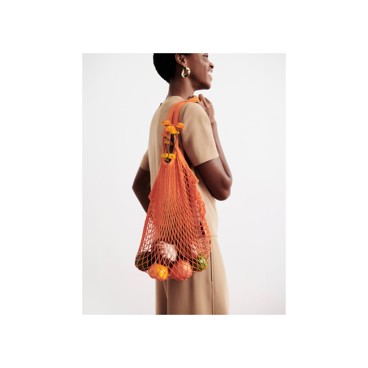 woman wearing light saddle short-sleeve Annika top and carrying orange bag of fruit over her shoulder