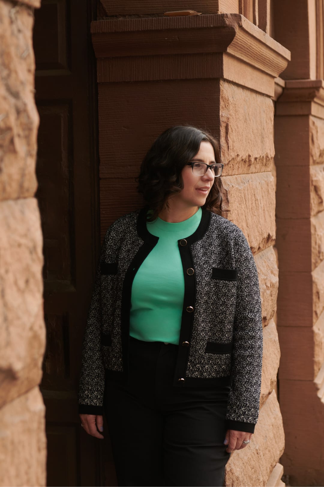Catherine Carlson standing in front of a brick pillar, wearing M.M.Lafleur seafoam green T-shirt and knit Evangeline jardigan
