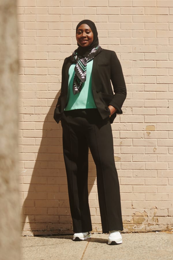 Batouly Camara M.S., wearing black hijab, black M.M.LaFleur blazer, seafoam green T-shirt, black pants, and black/white/seafoam icon print scarf tied around her neck
