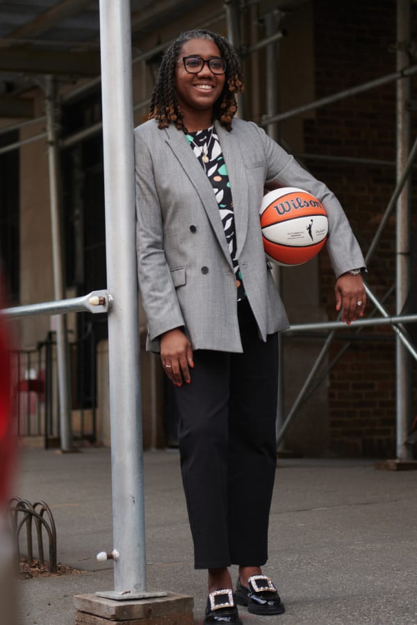 Keia Clarke smiling and holding a basketball and wearing M.M.LaFleur gray double-breasted blazer and black pants
