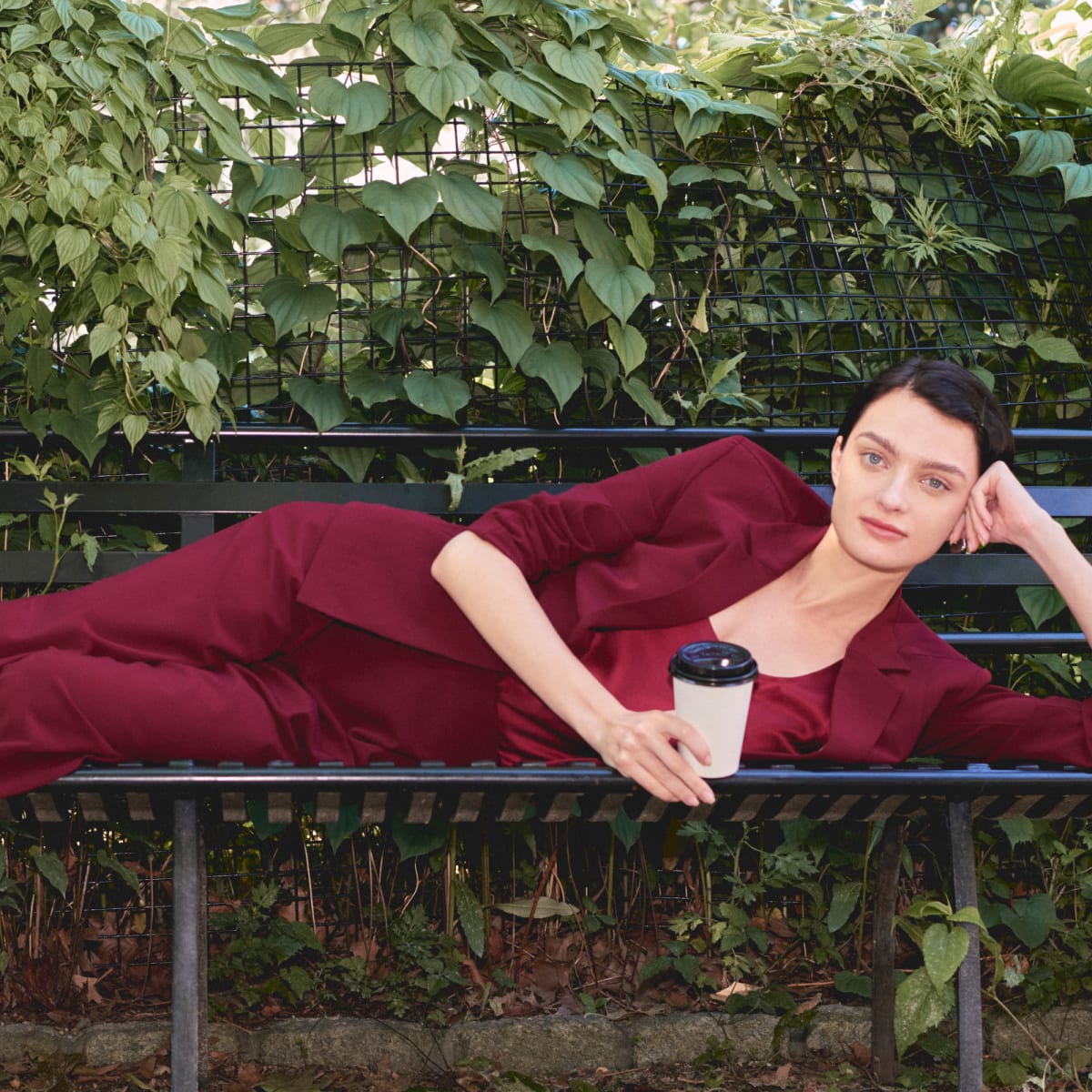 image of a woman laying on a bench holding a coffee cup