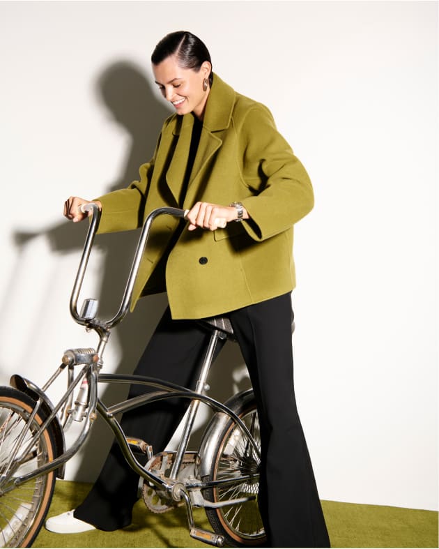 image of a woman wearing the callista coat in pistachio riding a bike