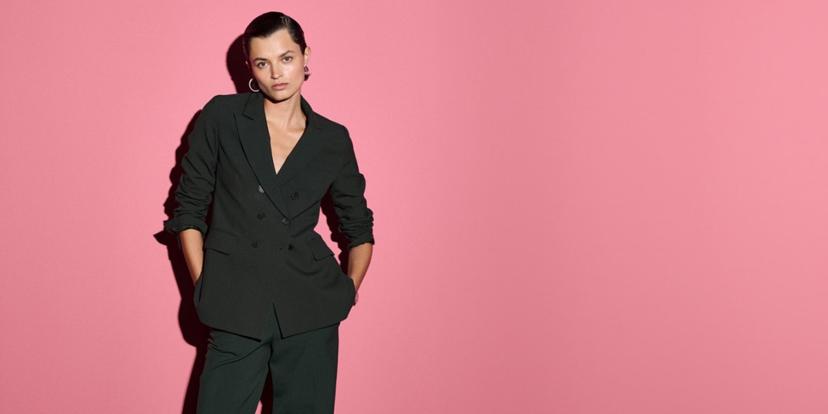 Image of a woman in a dark emerald suit against a pink background