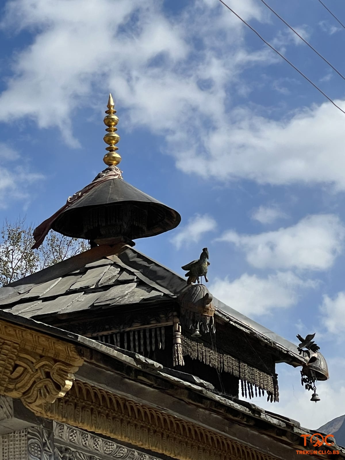 Golden temple spire and traditional slate roofing of the village shrine against mountain skies