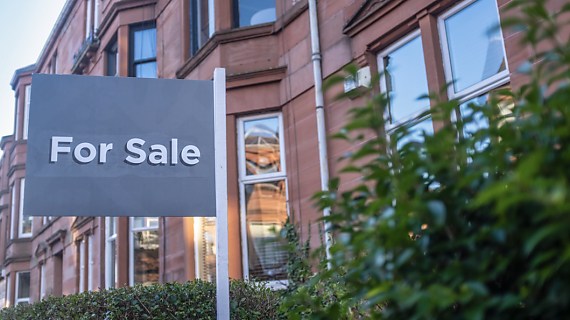 A residential house with a 'for sale' sign in the front yard