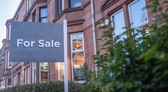 A residential house with a 'for sale' sign in the front yard