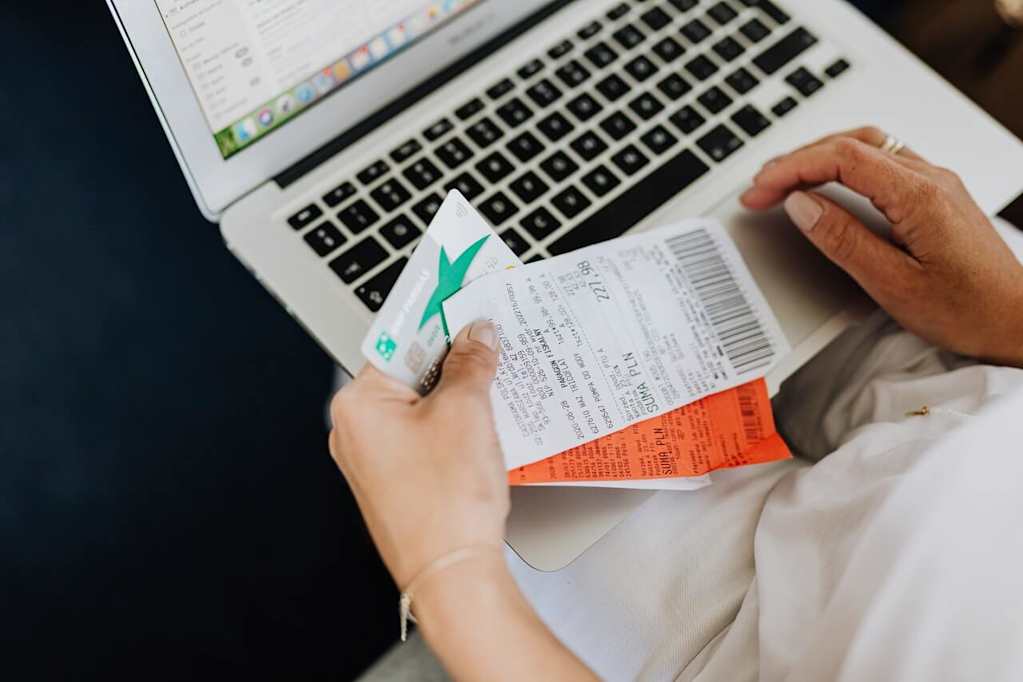 Woman holding receipts and credit card while using laptop