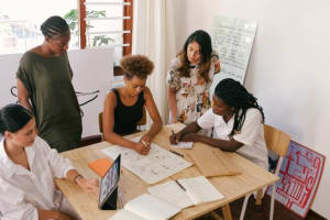 Group of colleagues working around a table using a notebook, paper, and a tablet.