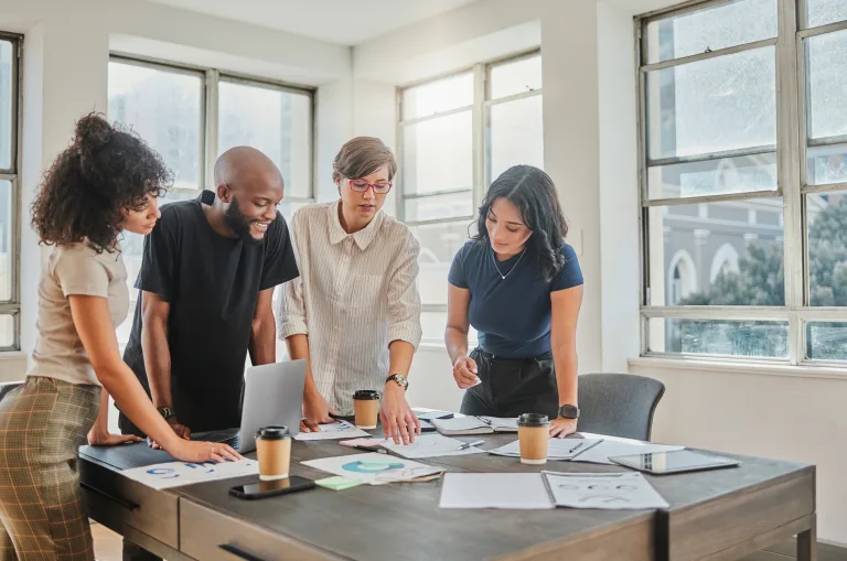 Four people looking at a table full of papers and coffee cups