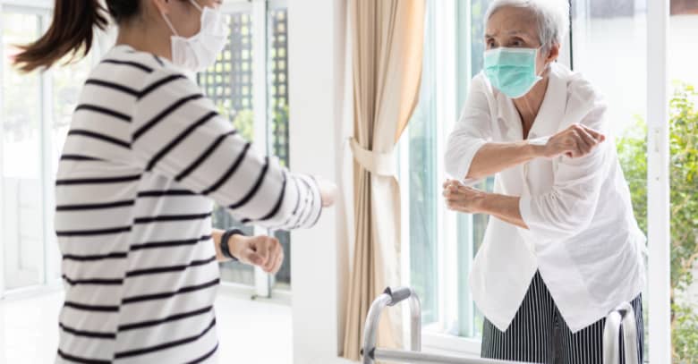 A caregiver and a senior both wear masks as the caregiver helps the senior with her daily exercises