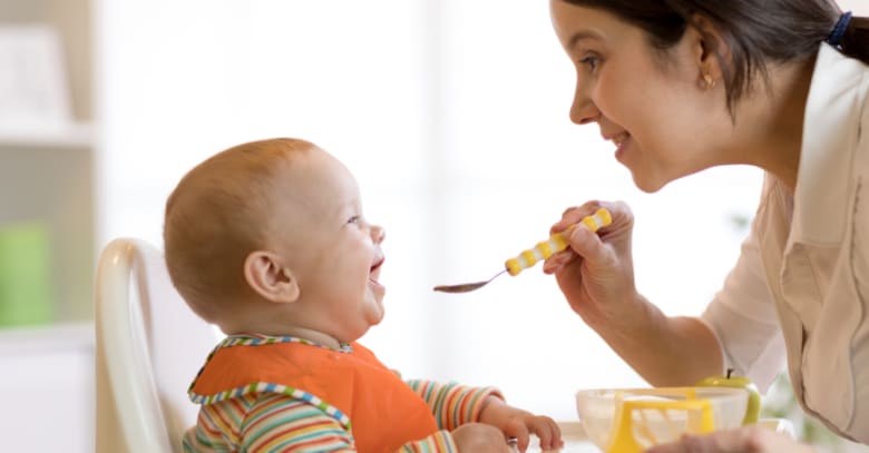 A baby is fed lunch by her nanny