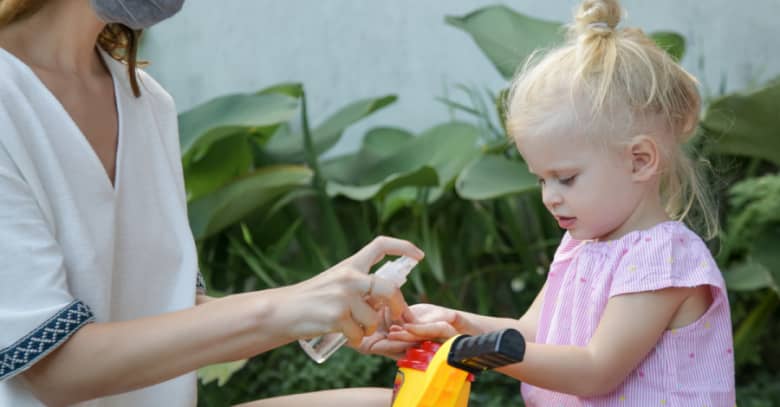 a child care provider dispenses hand sanitizer to a preschooler riding a tricycle