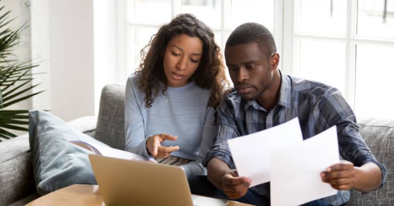 A young couple discusses their finances and budget while looking at their computer