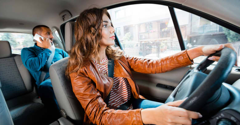 A woman drives a rideshare vehicle while a passenger sits in the backseat