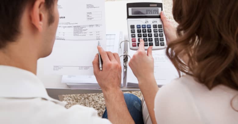 A couple is shown from behind using a calculator and reviewing their monthly bills