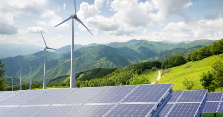 A building with solar panels is seen with windmills in the background