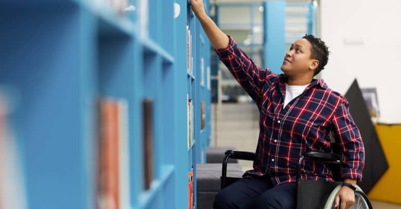 A college student who uses a wheelchair chooses books in the campus library