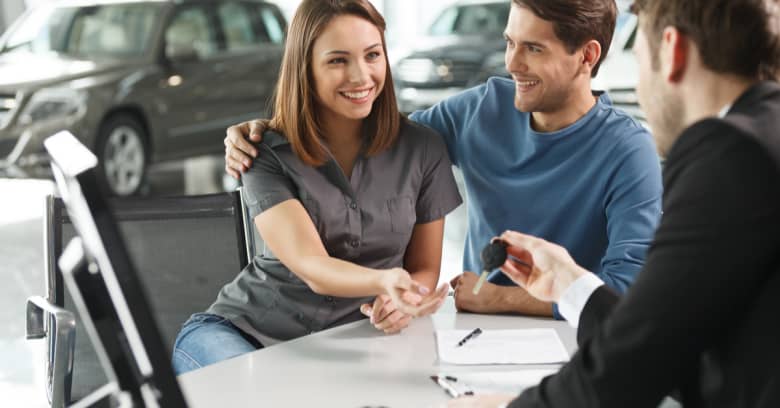 A young couple looks happy as they meet with a car salesperson to discuss their car-buying options