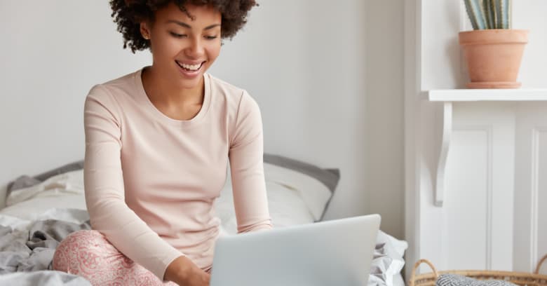 A young woman sits on her bed as she looks at insurance rates on her computer