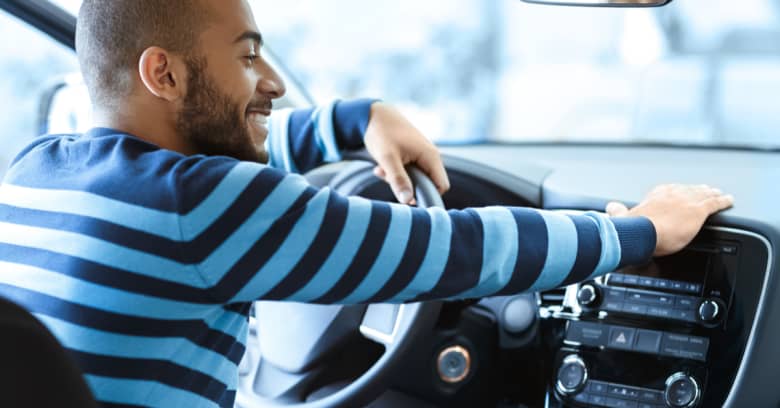 A smiling man sits in his new car and admires it