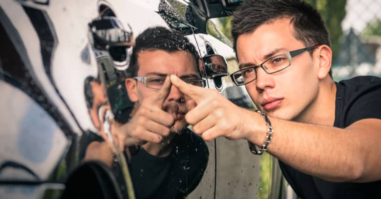 a young man inspects a used car he is considering purchasing