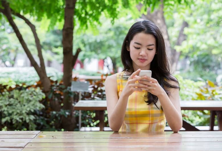 A woman sits at a picnic table outside and looks at her phone.