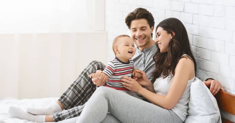 A couple and their baby lounge together at home in pajamas.