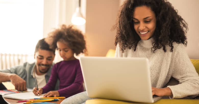 A woman looks into suspending her car insurance using her computer while her family is seen in the background