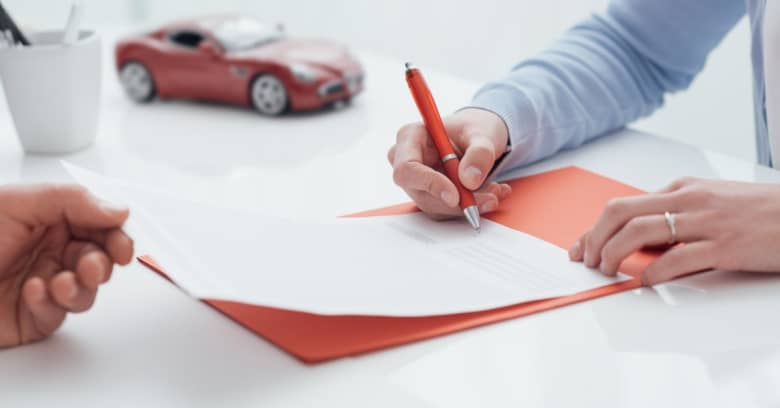 A young woman is signing documentation for her car loan. 