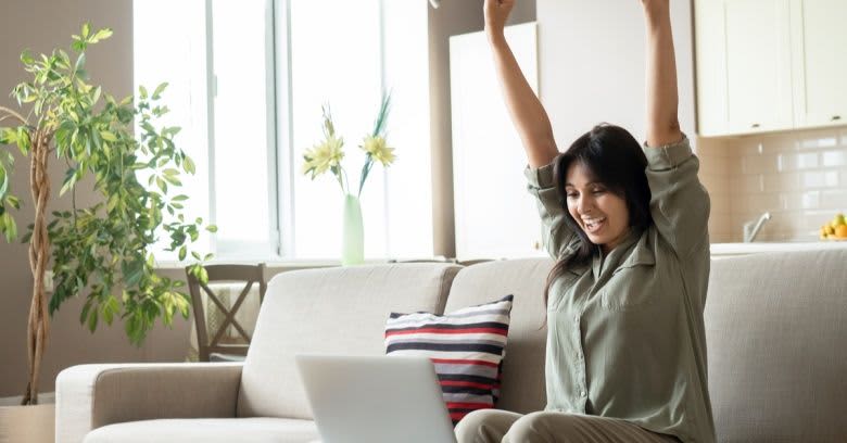 A woman celebrates while looking at her computer.