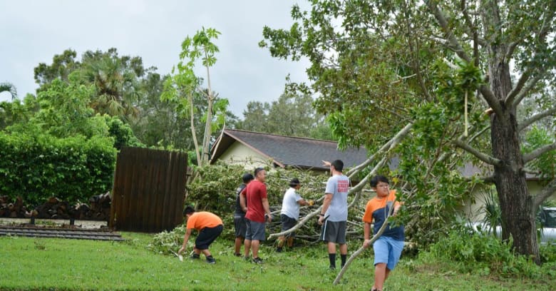 A group of neighborhood helpers remove debris from a yard after a hurricane