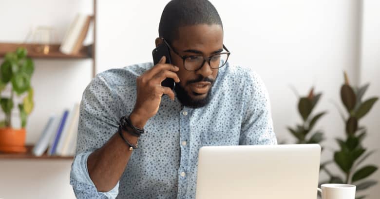 a concerned man is looking at his computer and having an animated phone conversation