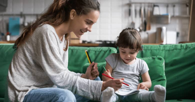 a woman and a little girl are sitting on the couch drawing pictures