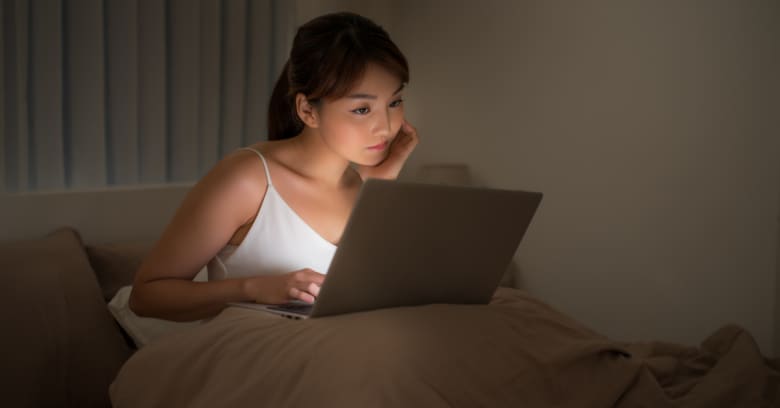 a woman looks at her computer in the dark while her computer screen can be seen glowing