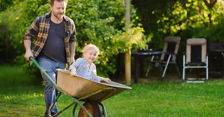 a man pushes his son in a wheelbarrow in the backyard