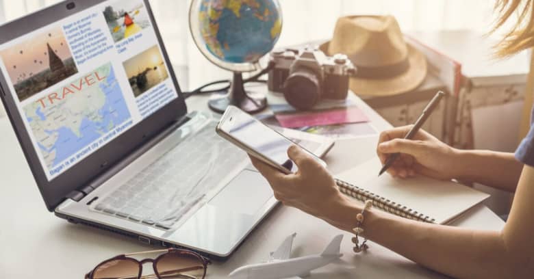 A woman makes updates to her travel plans using a computer and smart phone.